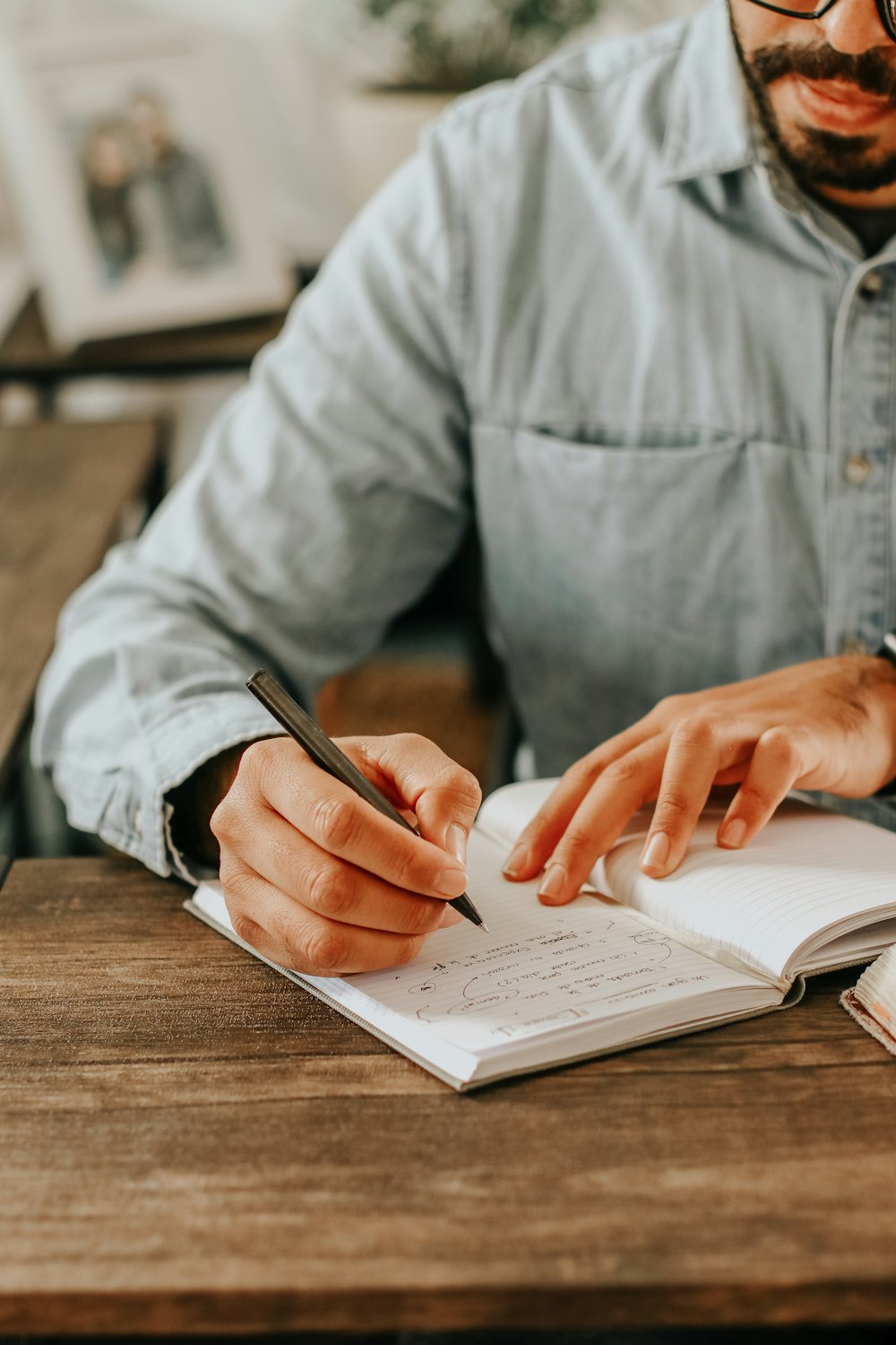 A man writes in a notebook at a wooden table at home
