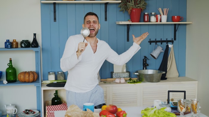 A man playfully singing into a kitchen ladle while cooking