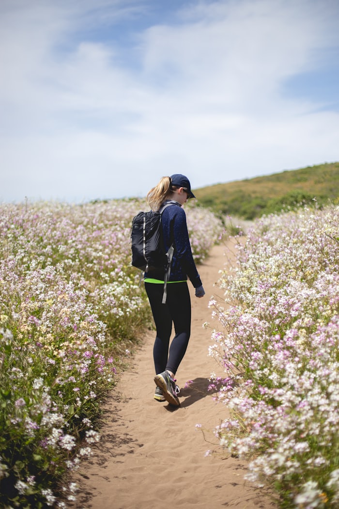 A woman walking a trail between wildflower fields